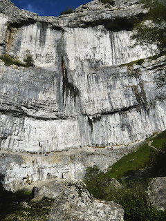 White limestone cliff face at Malham Cove with rocky slope and patches of grass