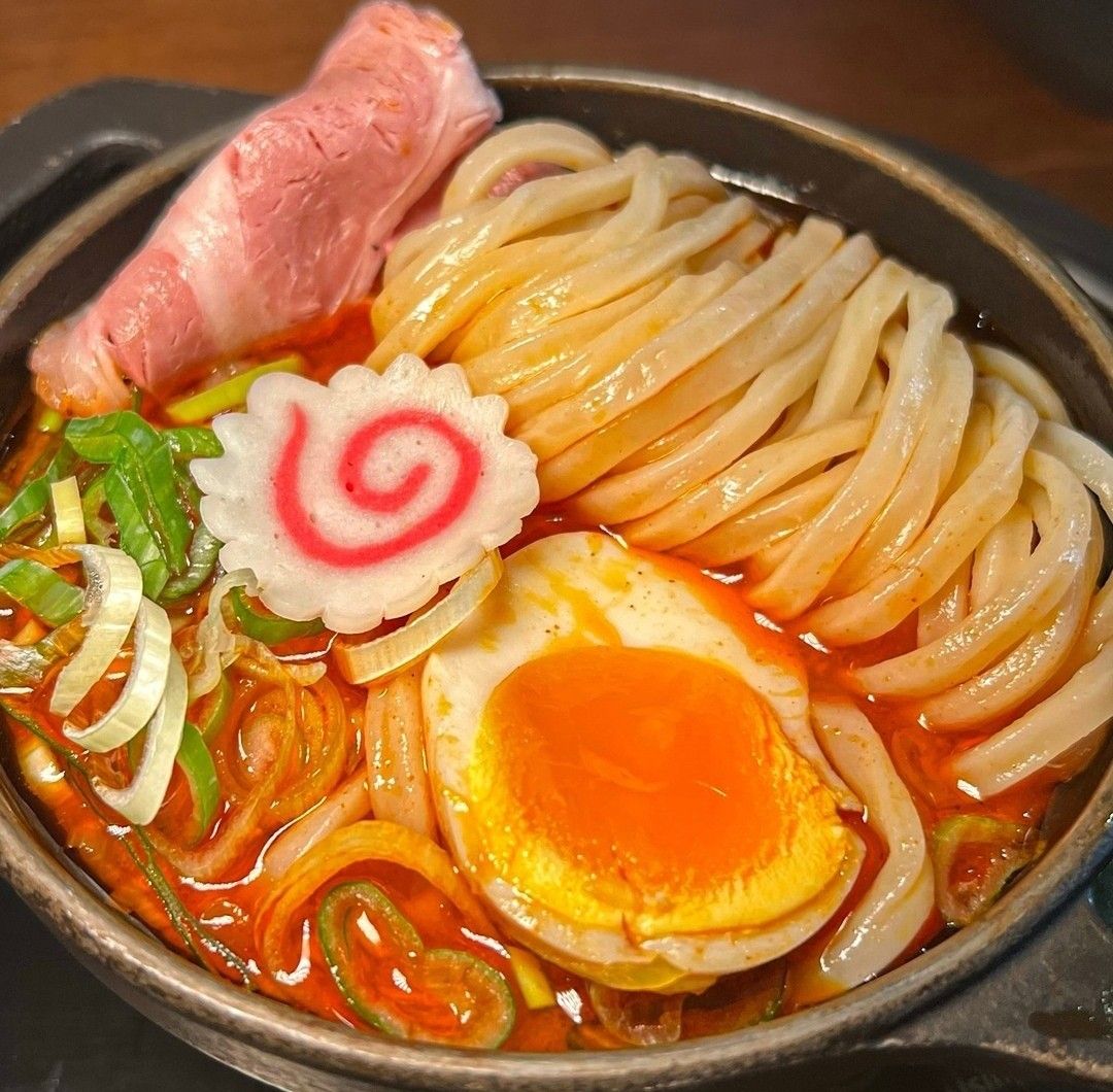 Close-up of a ramen bowl with noodles, pork, egg, green onions, and fish cake