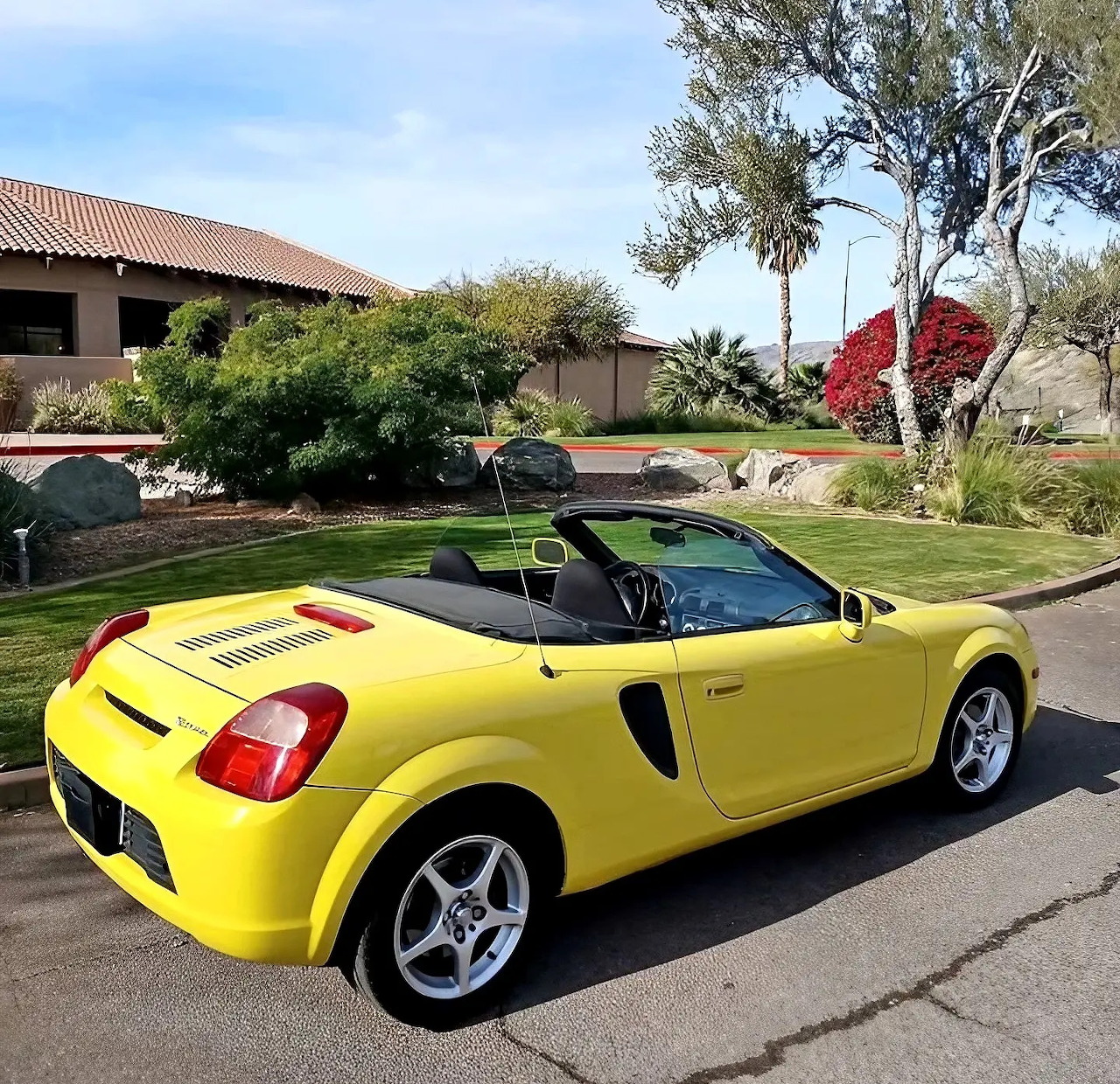 Yellow Toyota MR2 Spyder convertible parked on suburban street with palm trees