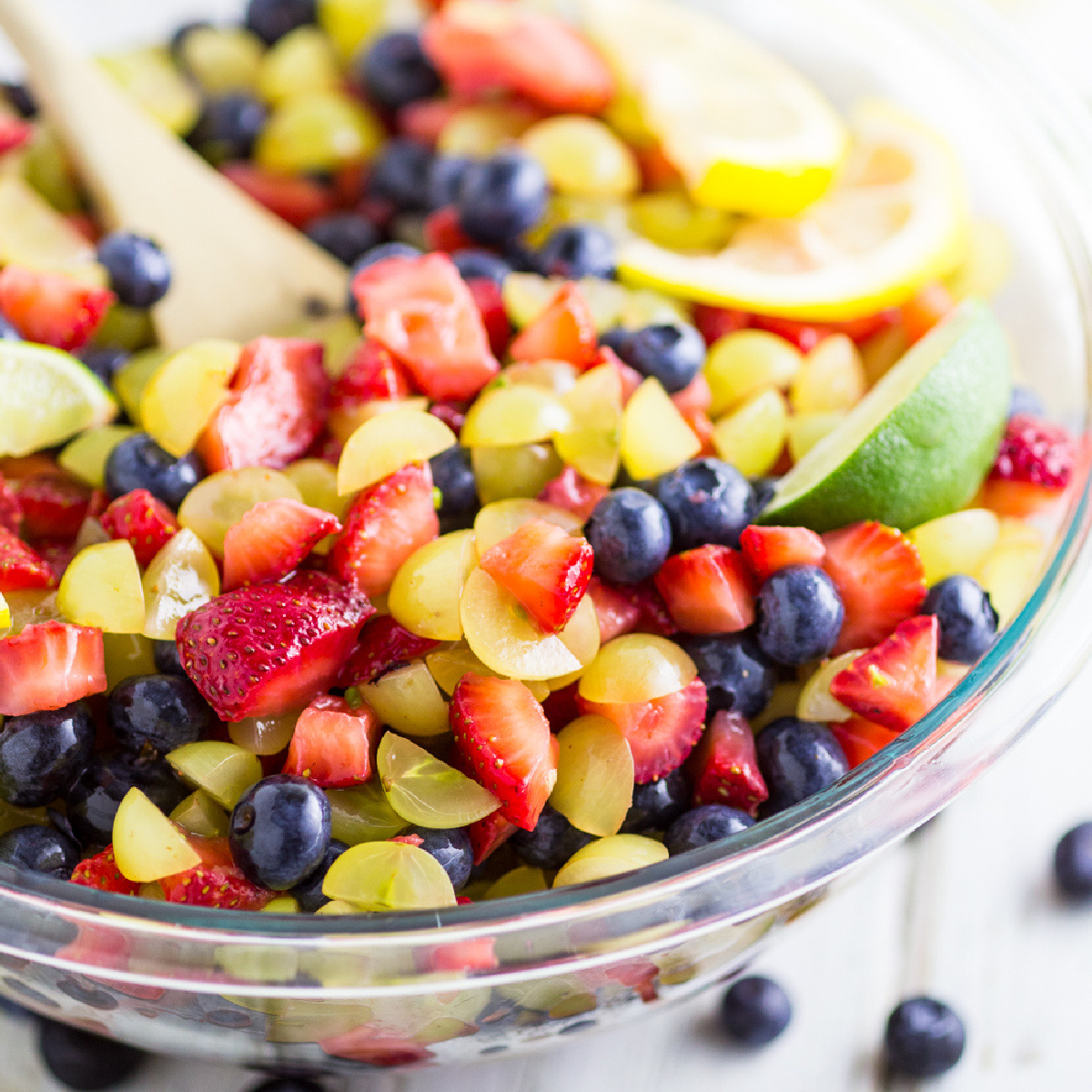 Glass bowl of mixed fruit salad with strawberries, blueberries, grapes, and pineapple