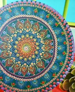 Circular mandala artwork with dots in blue, coral, yellow, and pink arranged in radiating geometric patterns
