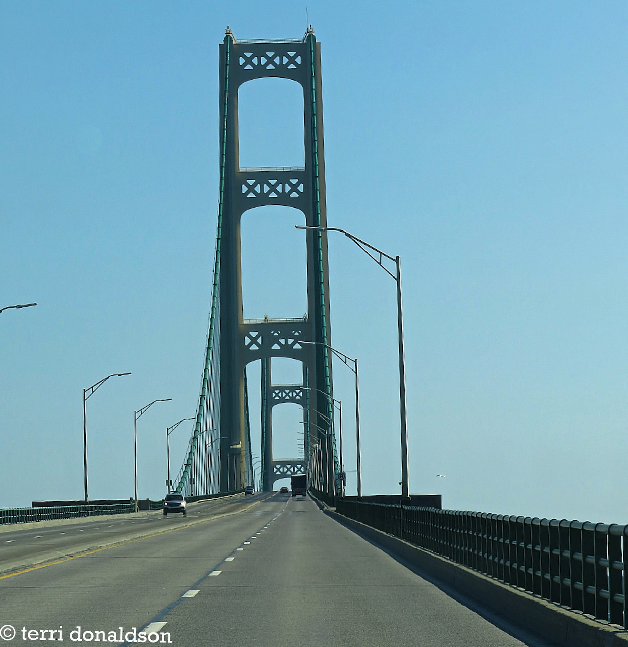 Roadway crossing the Mackinac Bridge with tall towers under a clear blue sky