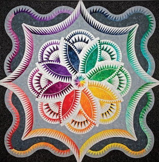 Colorful quilted wall hanging with rainbow star medallion and feathered decorative edges on grey fabric
