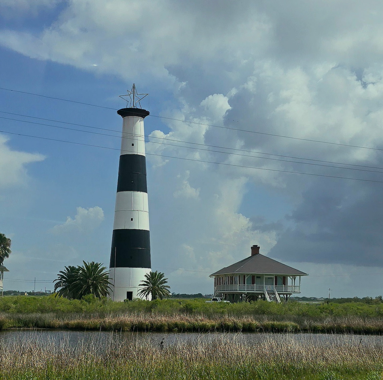 Tall black and white striped lighthouse next to historic keeper's house on coastal marshland
