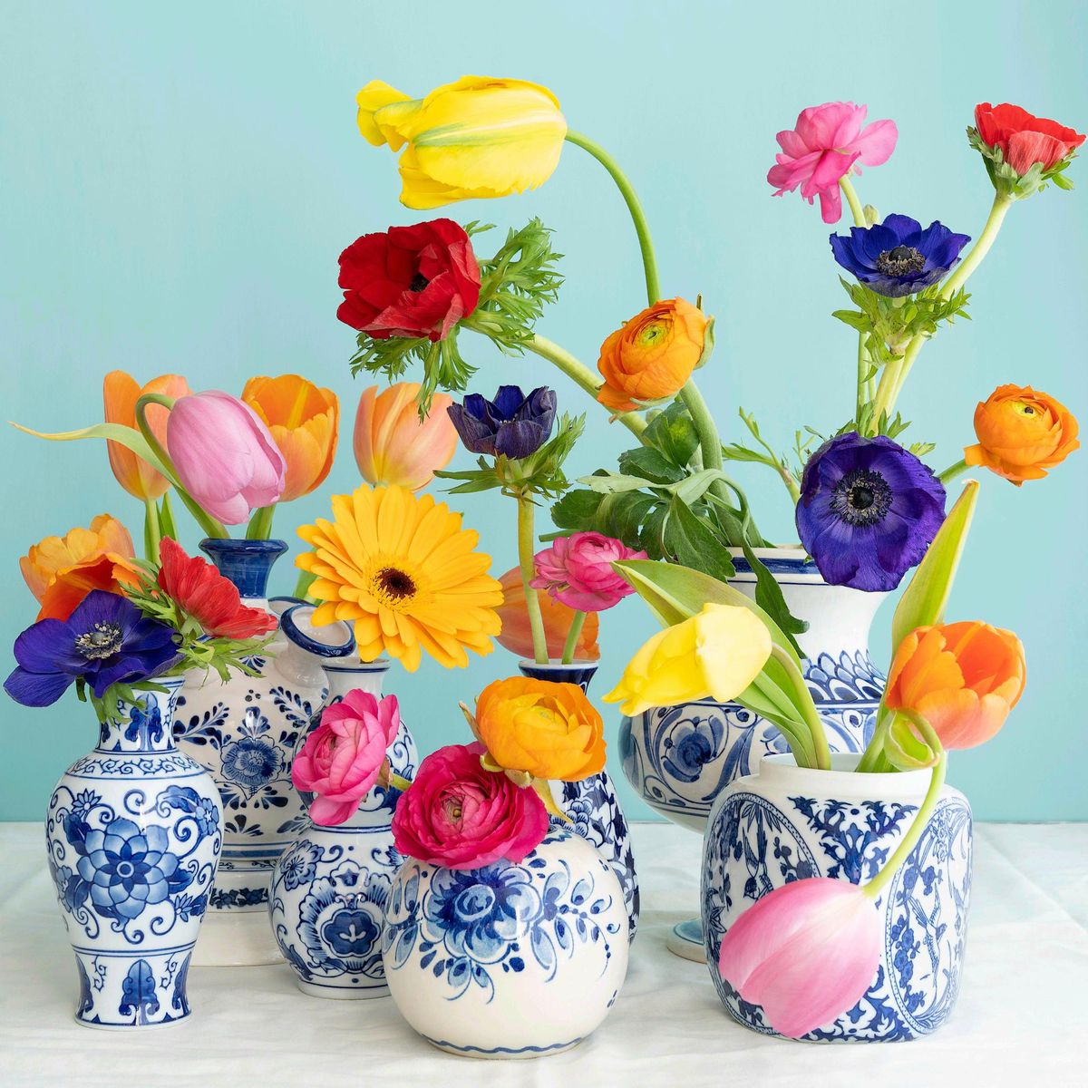 Colorful spring flowers arranged in ornate blue and white ceramic vases on white surface