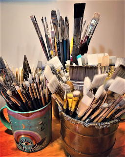 Assorted paint brushes in colorful containers on orange table