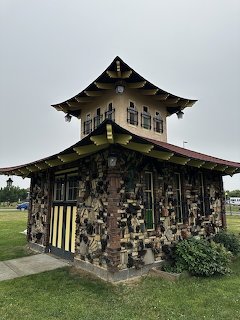 Small pagoda-style building covered in decorative objects and artwork, surrounded by green grass