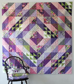 Purple geometric patchwork quilt hanging on a wall above a chair