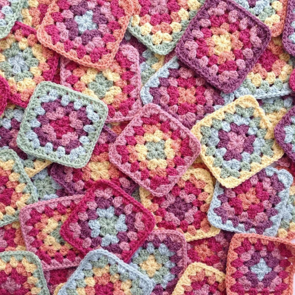 Overlapping colorful crochet granny squares in pink, yellow, blue and white yarn