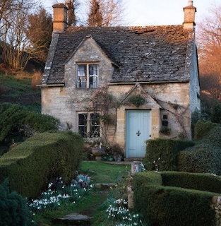 Stone cottage with blue door and sculpted garden at sunset