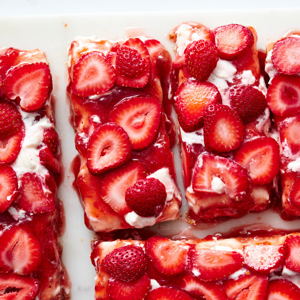 Strawberry pretzel bars topped with sliced fresh strawberies and cream on a white background
