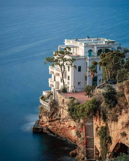 White villa on a rocky coastal cliff above deep blue sea in Posillipo, Italy
