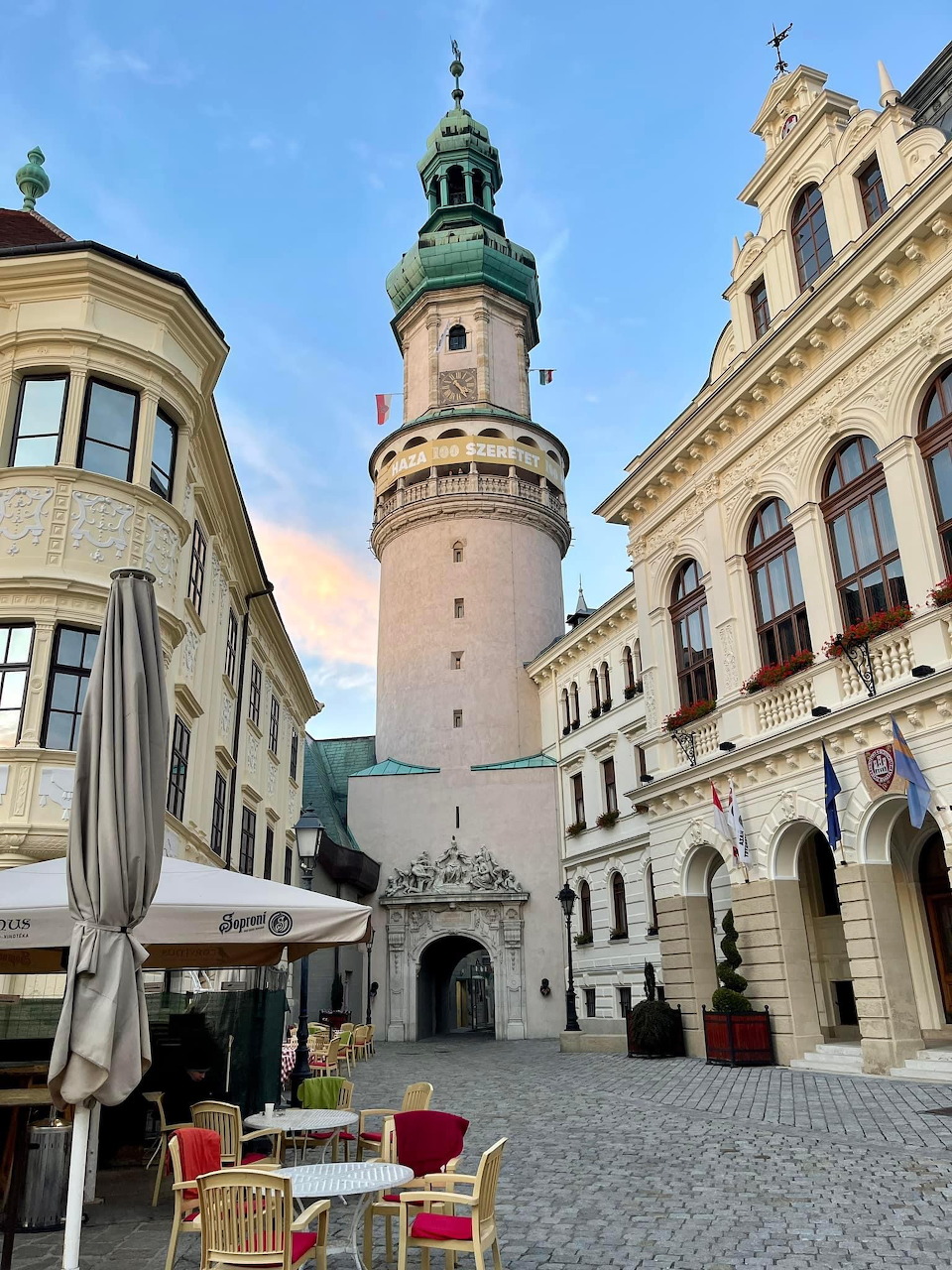 Tall stone fire tower with green dome rising between baroque buildings in Sopron town square
