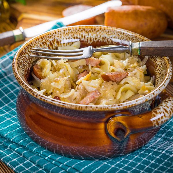 Rustic bowl of lazanki pasta with cabbage and sausage on a blue checkered cloth