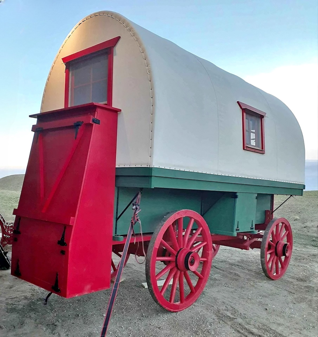 Vintage sheep wagon with white arched roof, bright pink door, turquoise body, and red wooden wagon wheels
