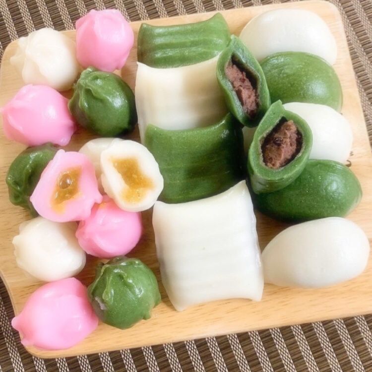 Colorful Korean rice cakes in green, white, and pink with red bean and other fillings on a wooden plate