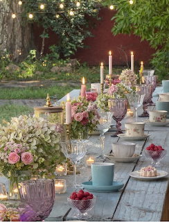 Elegant outdoor table set with candles, flowers, teacups, and berries in a garden