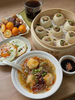 Overhead view of Asian food spread with steamed buns, dumplings,fried egg, kumquats, and dipping sauces