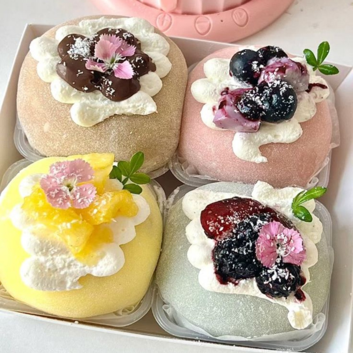 Four colorful square mochi topped with cream and fresh berries on a tray