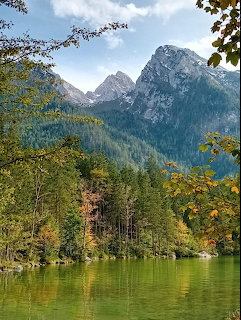 Alpine lake with green water surrounded by trees with autumn foliage and rocky mountain peaks behind