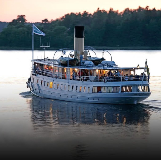 White vintage steamship on calm water at dusk near a dark tree-lined shore