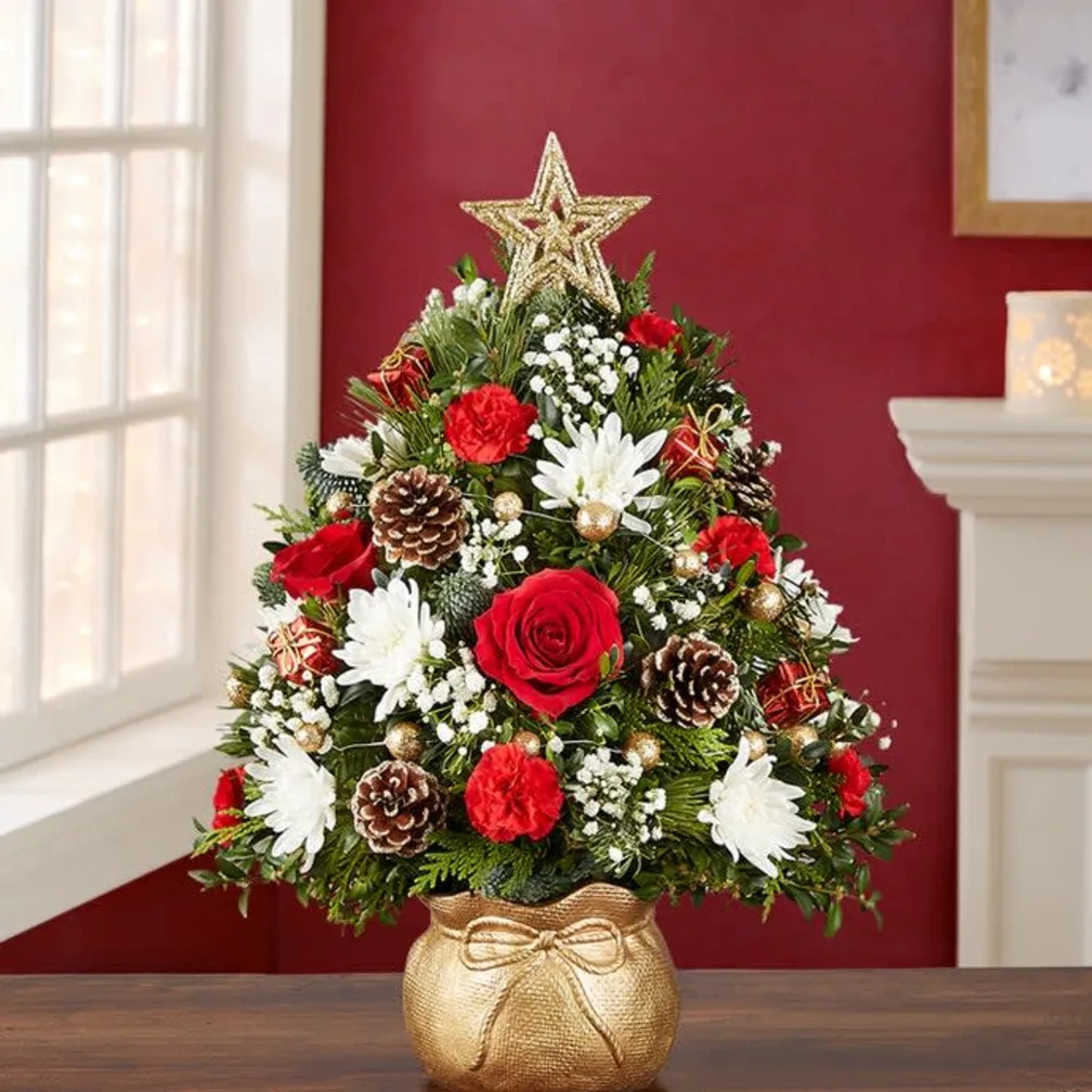 Christmas tree floral arrangement with red roses, white flowers, pine cones, and gold star in decorative gold pot