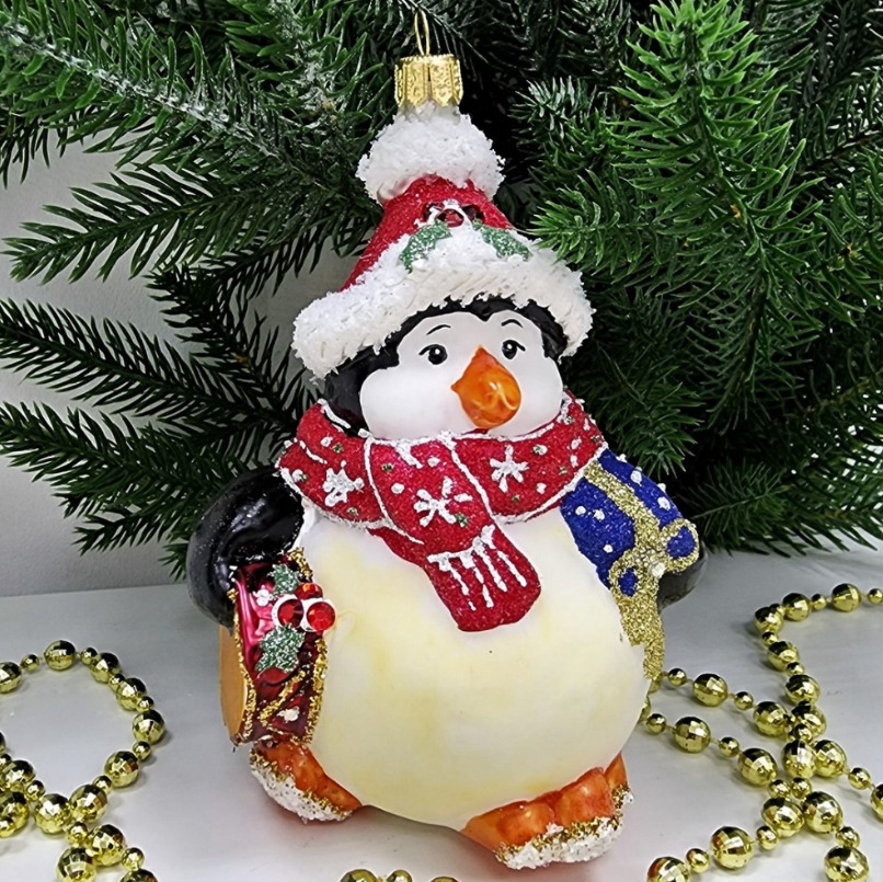 Decorative glass penguin ornament wearing Santa hat and red scarf, holding a blue gift box
