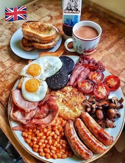 Full English breakfast plate with eggs, bacon, sausages, beans, and toast alongside a cup of tea