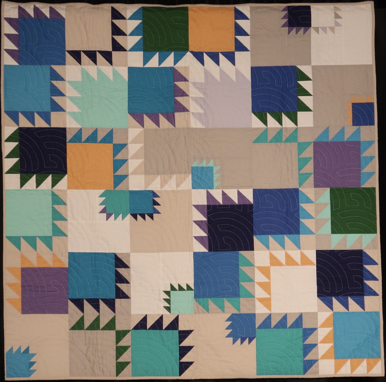 Quilt with geometric star pattern blocks in blue, green, orange and purple on cream fabric