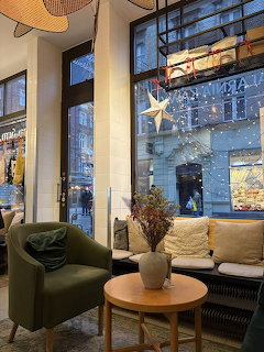 Modern cafe seating area with green chairs, wooden table, and large windows showing city view