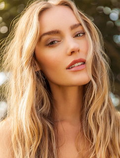 Close-up portrait of a blonde woman with wavy hair and natural makeup outdoors