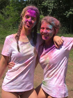 Two women outdoors wearing white shirts covered in colorful powder