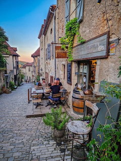 Cobblestone village street with café tables and stone buildings at dusk