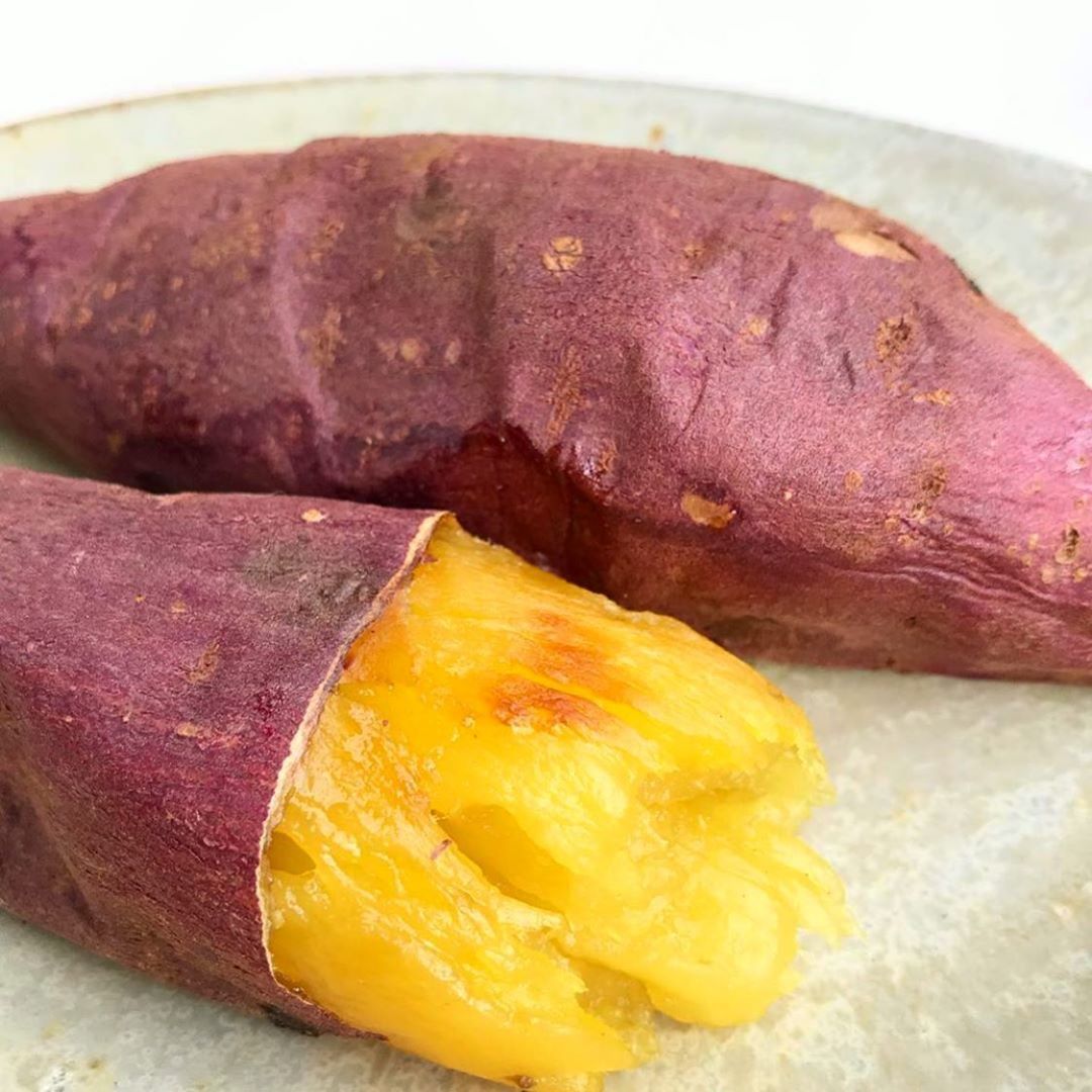 Two baked sweet potatoes on a plate, one broken open showing yellow flesh