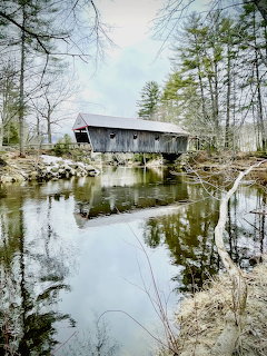 Gray covered bridge over a reflective river surrounded by bare trees