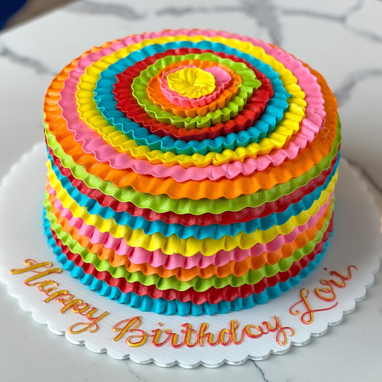 Colorful rainbow ruffle birthday cake on a white cake board with Happy Birthday icing