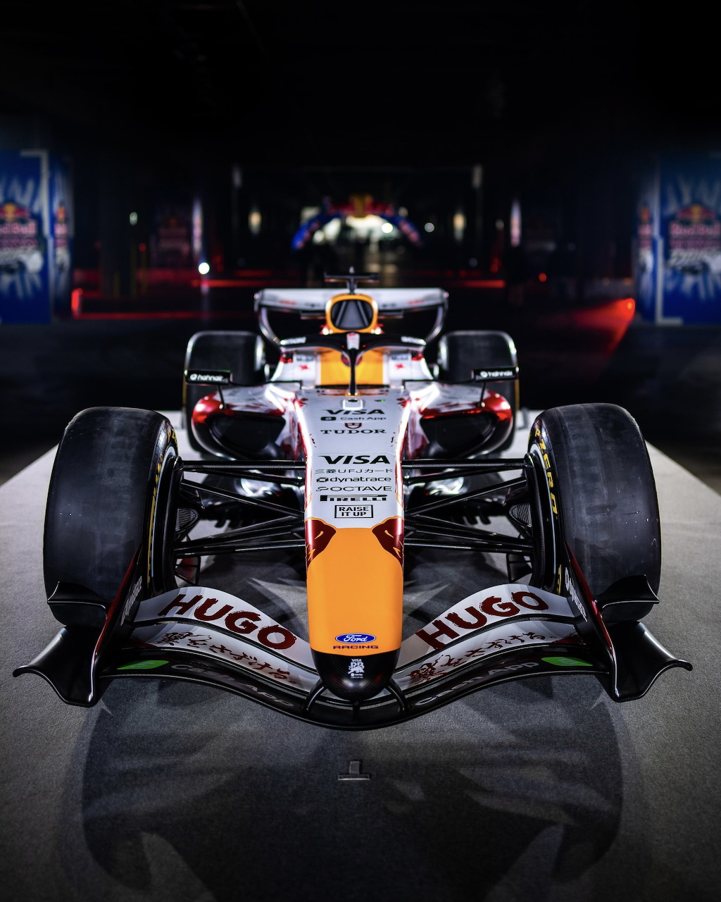 McLaren Formula 1 car with orange and black Hugo livery, front-facing view in dramatic dark lighting