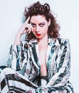 Woman with curly brown hair and red lipstick wearing a sequined striped blazer posing for a portrait
