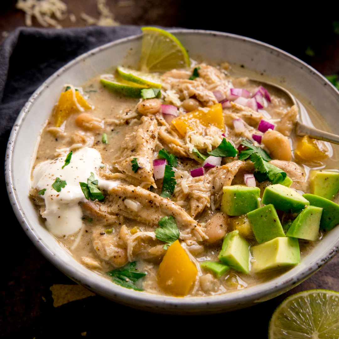 Bowl of creamy chicken soup with avocado, red onion, cilantro, mango, and lime