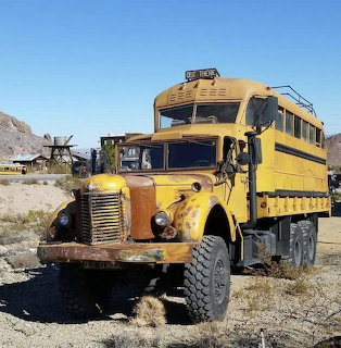 Old yellow school bus in desert setting with mountain backdrop
