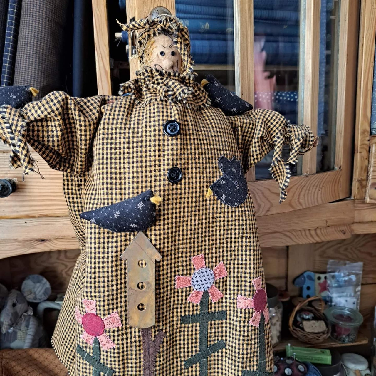 Handmade fabric doll in checkered pattern with buttons and flower decorations on wooden table