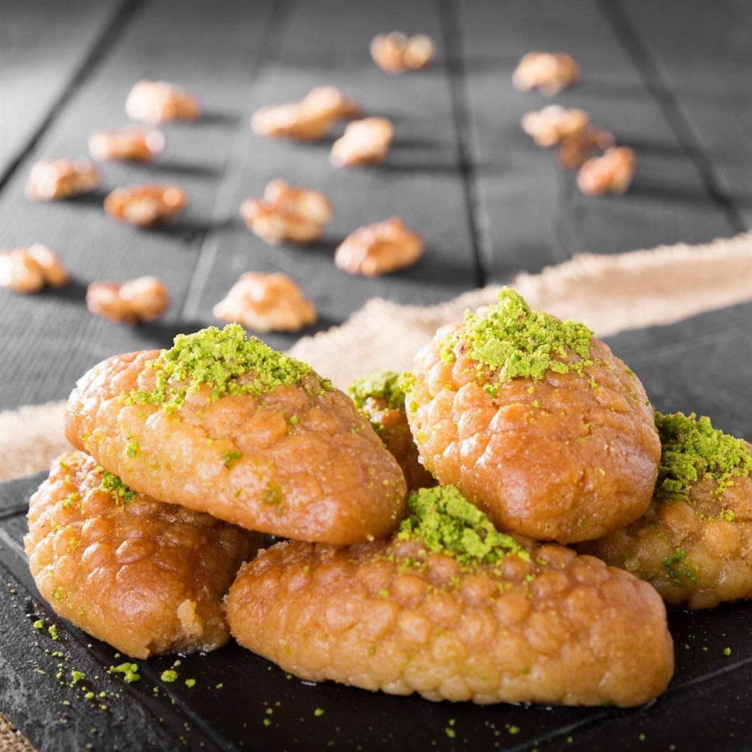 Fried tulumba pastries with green pistachio topping on dark slate surface
