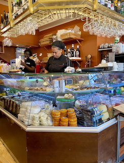 Cafe worker behind pastry display counter with hanging wine glasses overhead