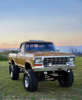 Lifted vintage Ford pickup truck parked on grass at sunset