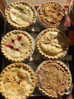 Six homemade pies with different crusts cooling on wire racks viewed from above