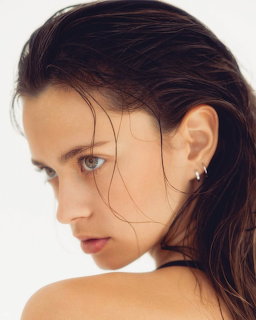 Close-up portrait of a woman with wet dark hair looking over her bare shoulder