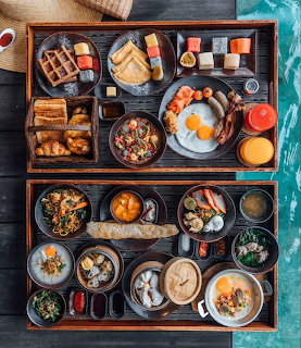 Overhead flatlay of two wooden trays with various brunch foods and drinks on dark table