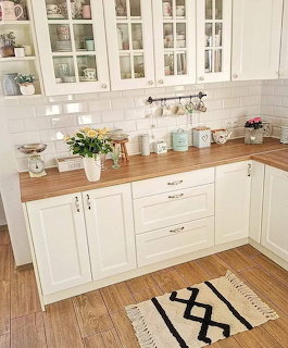 White farmhouse kitchen with wood counters, subway tile, glass cabinets, and geometric rug
