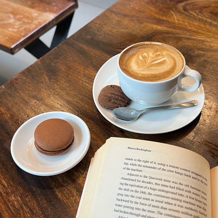 Latte with cookies, a macaron, and an open book on a wooden cafe table