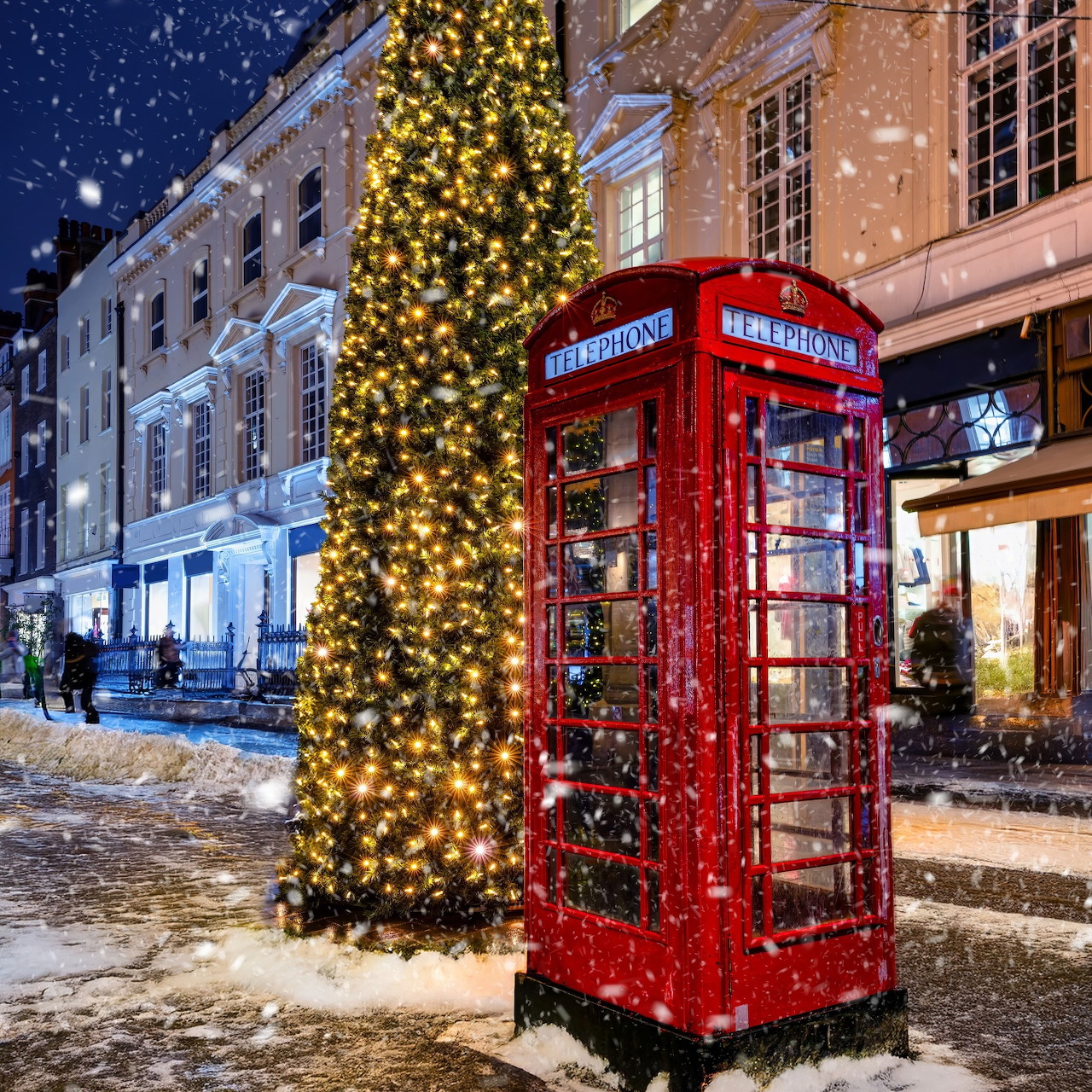 Red London phone box with Christmas lights and snow on snowy street at night